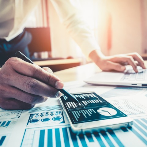 Hombre revisando datos financieros en computadora y celular, para el curso de Finanzas para no Financieros de la USFQ