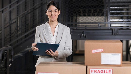 Mujer profesional supervisando mercancías con portapapeles de documentos, para el curso de Comercio y Logística Global de la USFQ