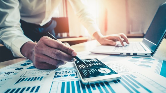 Hombre revisando datos financieros en computadora y celular, para el curso de Finanzas para no Financieros de la USFQ